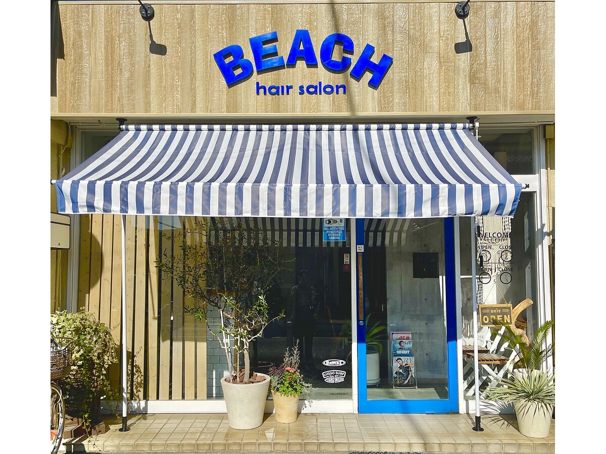 hair salon BEACHの外観。ブルーの手書きロゴと青白ストライプのオーニングが目印