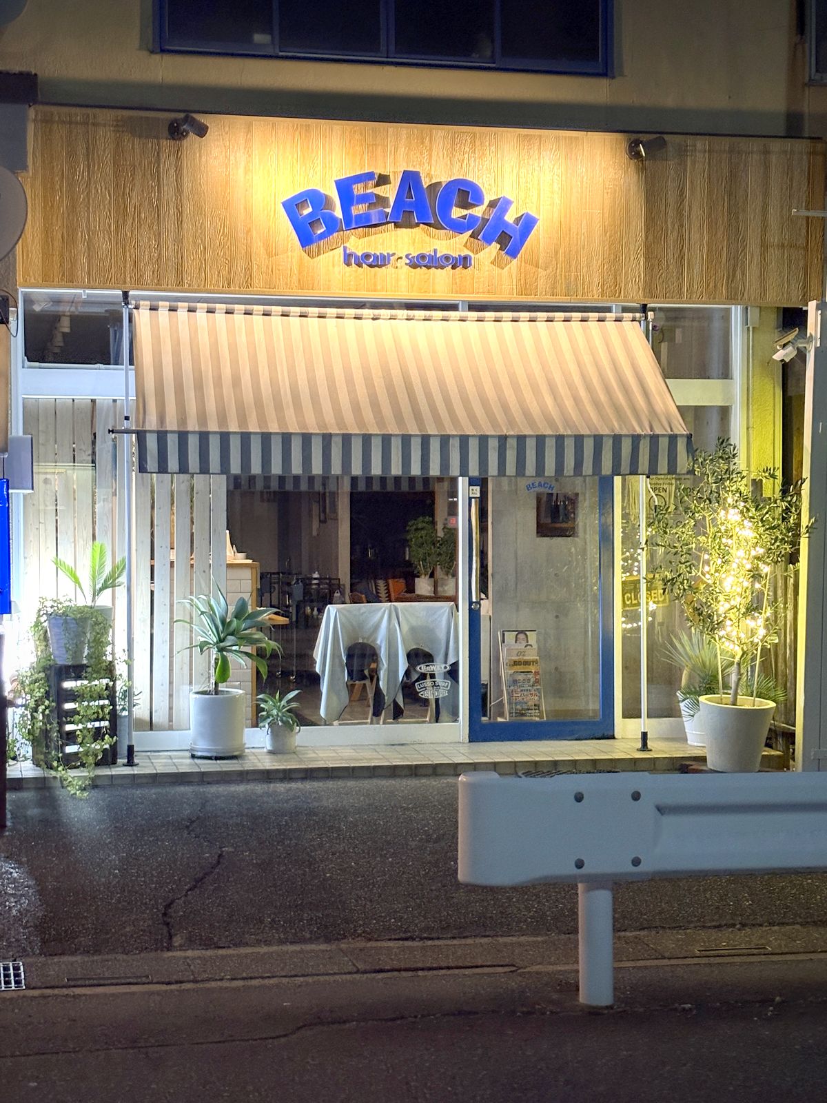 通りから見た夜のhair salon BEACH。店先のオリーブにライトが灯る